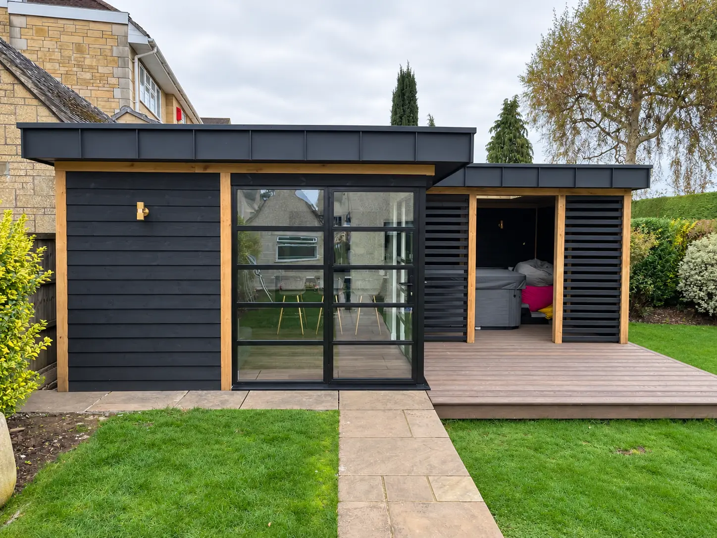 Front garden view of jet-black heritage aluminium doors on a timber-clad garden room
