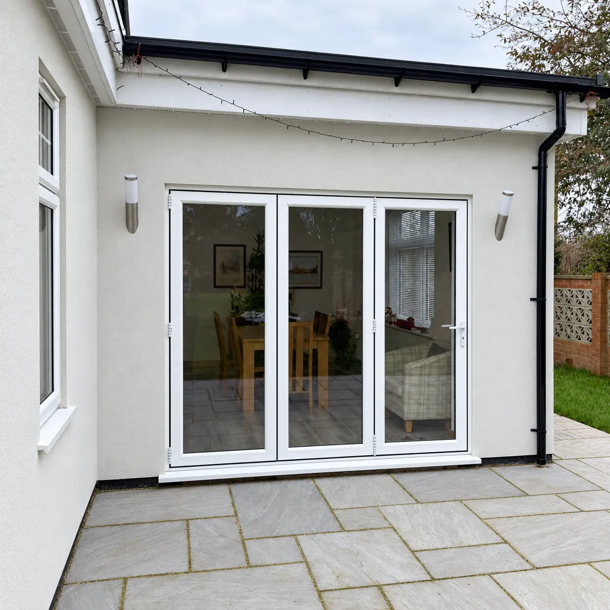 White three-panel bifold doors fitted to a rendered extension